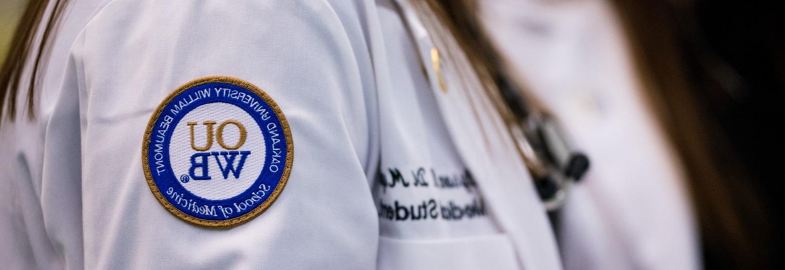 A close-up photo of a white coat with the OUWB patch in focus.